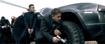 Movie still from “Hostage 911” (2018), directed by Robert Rodriguez – A man in a black suit sitting next to another man in a black suit; Medium shot, Low angle