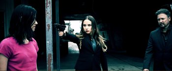 Movie still from “Hostage 911” (2018), directed by Robert Rodriguez – A beautiful woman holding a gun while wearing a suit and tie; Medium shot, Low angle