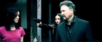 Movie still from “Hostage 911” (2018), directed by Robert Rodriguez – A woman holding a gun in front of a man; Medium shot, Over the shoulder angle