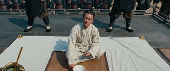 Movie still from “Red Cliff” (2008), directed by John Woo – A man sitting on the ground with a bowl in front of him; Medium shot, High angle