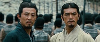 Movie still from “Red Cliff” (2008), directed by John Woo – Two asian men standing next to each other in front of a crowd of people; Close Up shot, Over the shoulder angle