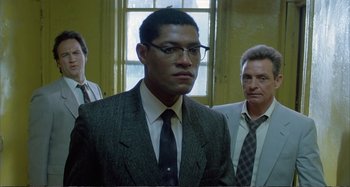 Movie still from “Red Heat” (1988), directed by Walter Hill – A man in a suit and tie standing next to two other men; Medium shot, Low angle