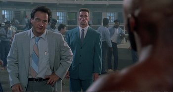 Movie still from “Red Heat” (1988), directed by Walter Hill – A man in a suit standing next to another man in a suit; Medium shot, Over the shoulder angle