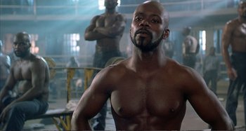 Movie still from “Red Heat” (1988), directed by Walter Hill – A man with a muscular body in a room; Medium shot, Low angle