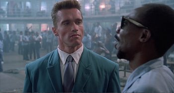 Movie still from “Red Heat” (1988), directed by Walter Hill – A man in a suit and tie next to another man in sunglasses; Close Up shot, Over the shoulder angle