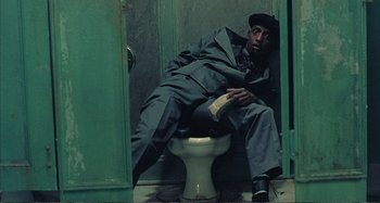 Movie still from “Red Heat” (1988), directed by Walter Hill – A man sitting on a toilet in front of a green door; Medium shot, Overhead angle