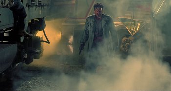 Movie still from “Red Heat” (1988), directed by Walter Hill – A man in a trench coat walking through a smoke filled street; Wide shot, Low angle