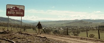 Movie still from “Red Hill” (2010), directed by Patrick Hughes – A person walking on a dirt road near a valley; Extreme Wide shot, High angle