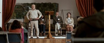 Movie still from “Red Hill” (2010), directed by Patrick Hughes – A man standing in front of a podium with people sitting in front of him; Wide shot, Low angle