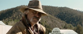 Movie still from “Red Hill” (2010), directed by Patrick Hughes – An older man wearing a hat standing in front of a sign; Close Up shot, Low angle