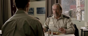 Movie still from “Red Hill” (2010), directed by Patrick Hughes – A man sitting at a table with a plate in front of him; Close Up shot, Over the shoulder angle