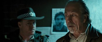 Movie still from “Red Hill” (2010), directed by Patrick Hughes – A man in a cowboy hat standing in front of a picture of a man; Close Up shot, Low angle