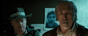 Movie still from “Red Hill” (2010), directed by Patrick Hughes – A person with a picture of a man in the background; Close Up shot, Over the shoulder angle
