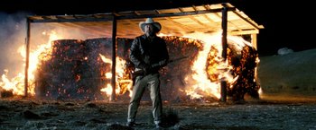 Movie still from “Red Hill” (2010), directed by Patrick Hughes – A man holding a rifle in front of a fire; Wide shot, Low angle