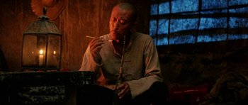 Movie still from “Red Sorghum” (1988), directed by Yimou Zhang – A man sitting in front of a bowl of food and holding chopsticks in his mouth; Medium shot, Low angle