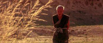 Movie still from “Red Sorghum” (1988), directed by Yimou Zhang – An older man in a brown robe standing in a field; Medium shot, Low angle