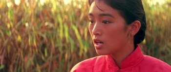 Movie still from “Red Sorghum” (1988), directed by Yimou Zhang – A young asian woman in a red shirt looking off into the distance; Close Up shot, Over the shoulder angle