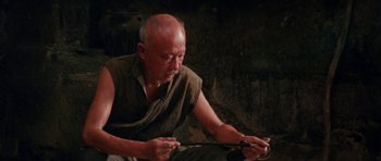 Movie still from “Red Sorghum” (1988), directed by Yimou Zhang – An older man sitting on the ground looking down at a pair of scissors; Medium shot, High angle