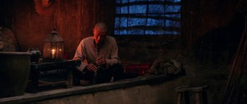 Movie still from “Red Sorghum” (1988), directed by Yimou Zhang – A man sitting on the ground playing a flute; Wide shot, Low angle