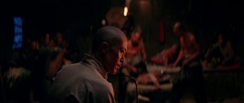 Movie still from “Red Sorghum” (1988), directed by Yimou Zhang – A man with a shaved head is speaking into a microphone; Medium shot, Over the shoulder angle