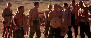 Movie still from “Red Sorghum” (1988), directed by Yimou Zhang – A group of men standing next to each other on a dirt field; Wide shot, Low angle