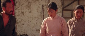 Movie still from “Red Sorghum” (1988), directed by Yimou Zhang – A woman in a pink shirt standing in front of a wall; Medium shot, Over the shoulder angle
