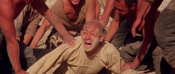 Movie still from “Red Sorghum” (1988), directed by Yimou Zhang – A man is being whipped by two other men; Medium shot, High angle
