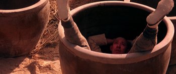 Movie still from “Red Sorghum” (1988), directed by Yimou Zhang – A man is in a clay pot with a stick in it; Wide shot, High angle