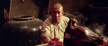 Movie still from “Red Sorghum” (1988), directed by Yimou Zhang – A man sitting at a table in front of a large amount of meat; Close Up shot, High angle