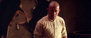 Movie still from “Red Sorghum” (1988), directed by Yimou Zhang – A bald man with a shaved head is standing in front of a wall; Close Up shot, Low angle