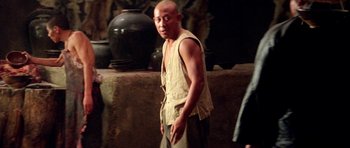 Movie still from “Red Sorghum” (1988), directed by Yimou Zhang – A man standing in front of a stone wall; Medium shot, Over the shoulder angle