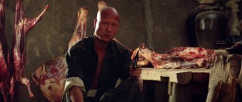 Movie still from “Red Sorghum” (1988), directed by Yimou Zhang – A man sitting in a room holding a knife; Medium shot, High angle