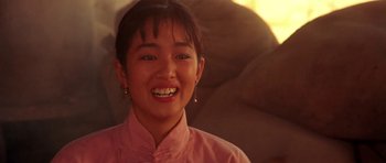 Movie still from “Red Sorghum” (1988), directed by Yimou Zhang – A young woman smiles for the camera in front of a stone wall; Close Up shot, Low angle