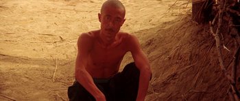 Movie still from “Red Sorghum” (1988), directed by Yimou Zhang – A man sitting on the ground with no shirt on; Medium shot, Low angle