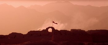 Movie still from “Red Sorghum” (1988), directed by Yimou Zhang – A red flag flying on top of an arch in front of mountains; Extreme Wide shot, Low angle