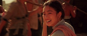Movie still from “Red Sorghum” (1988), directed by Yimou Zhang – A young woman smiles brightly while standing outside; Close Up shot, Over the shoulder angle
