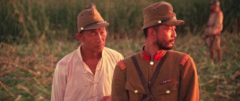 Movie still from “Red Sorghum” (1988), directed by Yimou Zhang – Two men in military uniforms are standing next to each other in a field; Close Up shot, Over the shoulder angle
