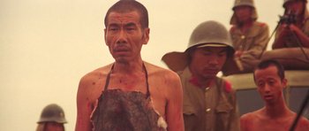 Movie still from “Red Sorghum” (1988), directed by Yimou Zhang – A man with no shirt standing next to another man in an army uniform; Medium shot, Low angle