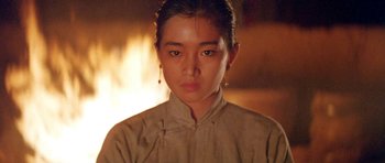 Movie still from “Red Sorghum” (1988), directed by Yimou Zhang – A young woman in a tan shirt is staring straight ahead; Close Up shot, Low angle