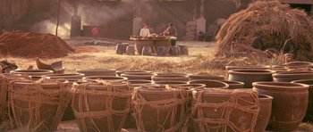 Movie still from “Red Sorghum” (1988), directed by Yimou Zhang – Two people sitting at a table in front of a bunch of pots; Extreme Wide shot, High angle