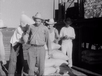 Movie still from “Redes” (1936), directed by Fred Zinnemann – A black and white photo of men standing next to a pile of bags; Medium shot, High angle