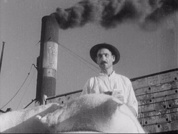 Movie still from “Redes” (1936), directed by Fred Zinnemann – An old man standing next to a building with smoke coming out of the chimney; Medium shot, Low angle