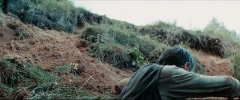 Movie still from “Redirected” (2014), directed by Emilis Velyvis – A man sitting on the ground in the grass; Medium shot, Low angle