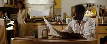 Movie still from “Reign Over Me” (2007), directed by Mike Binder – A man sitting at a kitchen table reading a newspaper; Medium shot, Over the shoulder angle