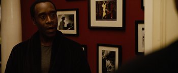 Movie still from “Reign Over Me” (2007), directed by Mike Binder – A man standing in front of a red wall with pictures on the wall behind him; Close Up shot, Over the shoulder angle