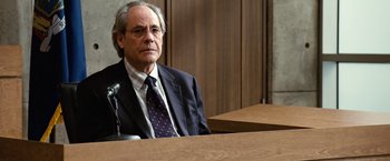 Movie still from “Reign Over Me” (2007), directed by Mike Binder – A man in a suit sitting in front of a microphone in a courtroom; Medium shot, Over the shoulder angle