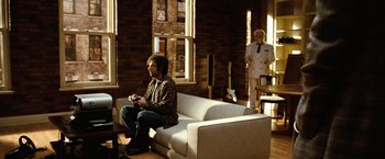 Movie still from “Reign Over Me” (2007), directed by Mike Binder – A man sitting on top of a white couch holding a nintendo wii game controller; Wide shot, Over the shoulder angle