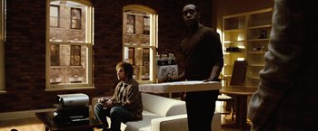 Movie still from “Reign Over Me” (2007), directed by Mike Binder – A man holding a tray of beer while another man sits on a white couch; Wide shot, Over the shoulder angle