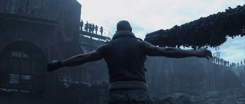 Movie still from “Reign of Fire” (2002), directed by Rob Bowman – A man standing on top of a building with arms outstretched; Medium shot, Low angle