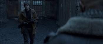 Movie still from “Reign of Fire” (2002), directed by Rob Bowman – A man holding a rifle in a dark alley; Medium shot, Over the shoulder angle
